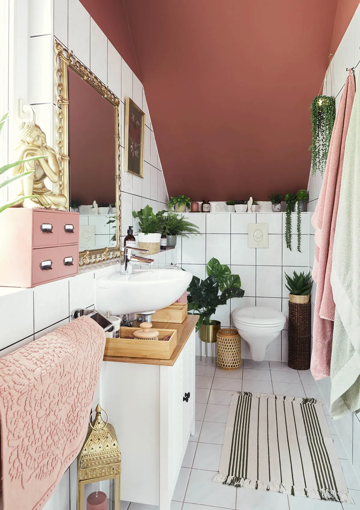 En suite bathroom,slited ceiling,rug,tiling,sink.mirror,storage,open shelving,plants