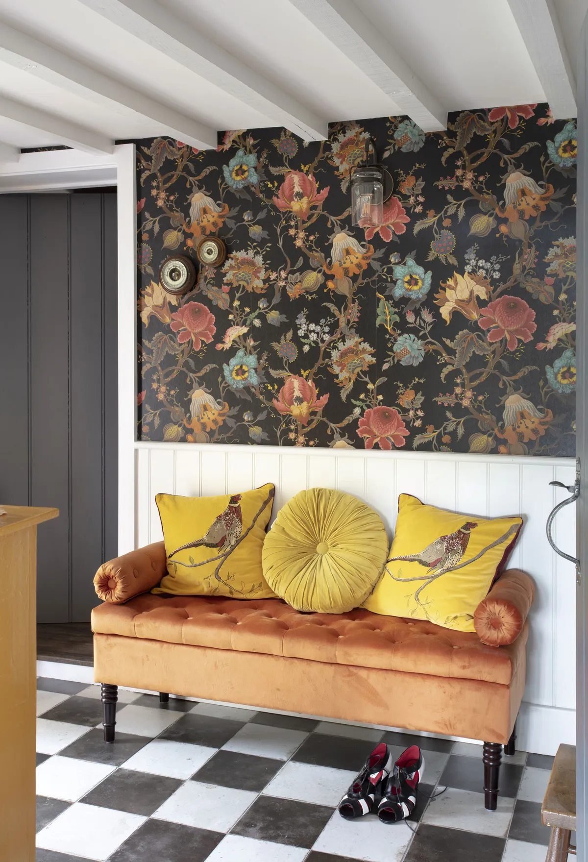 A handy seat fits snugly in the space between the door to the living room and a storage cupboard. Sabrina chose an exact orange shade from the wallpaper and added mustard cushions to make it cosy