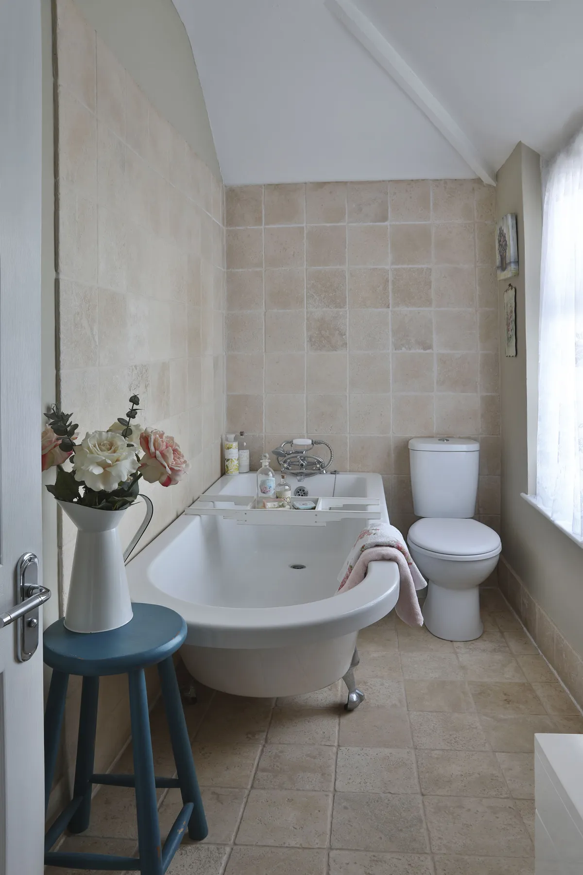 Hildah mixed modern with traditional in her bathroom with a single-ended rolltop bath from Victorian Plumbing, and Travertine tiles from Topps Tiles. An upcycled blue stool adds a splash of colour