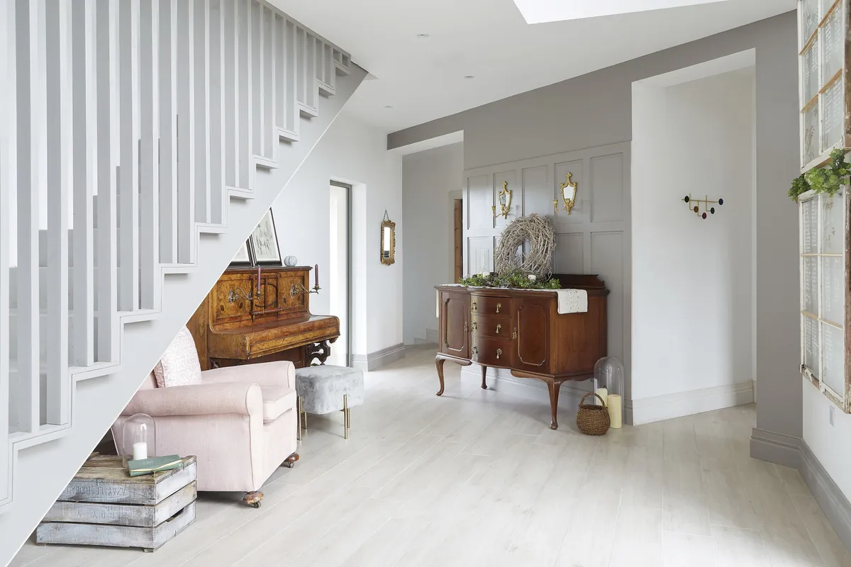 Mahogany tones add warmth to the pale-grey hallway. The piano was a gift from their architect, and Gillian has paired it with a velvet stool for a modern twist