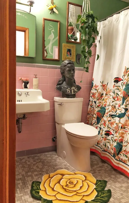 Pink tiled bathroom with floral shower curtain and antiques
