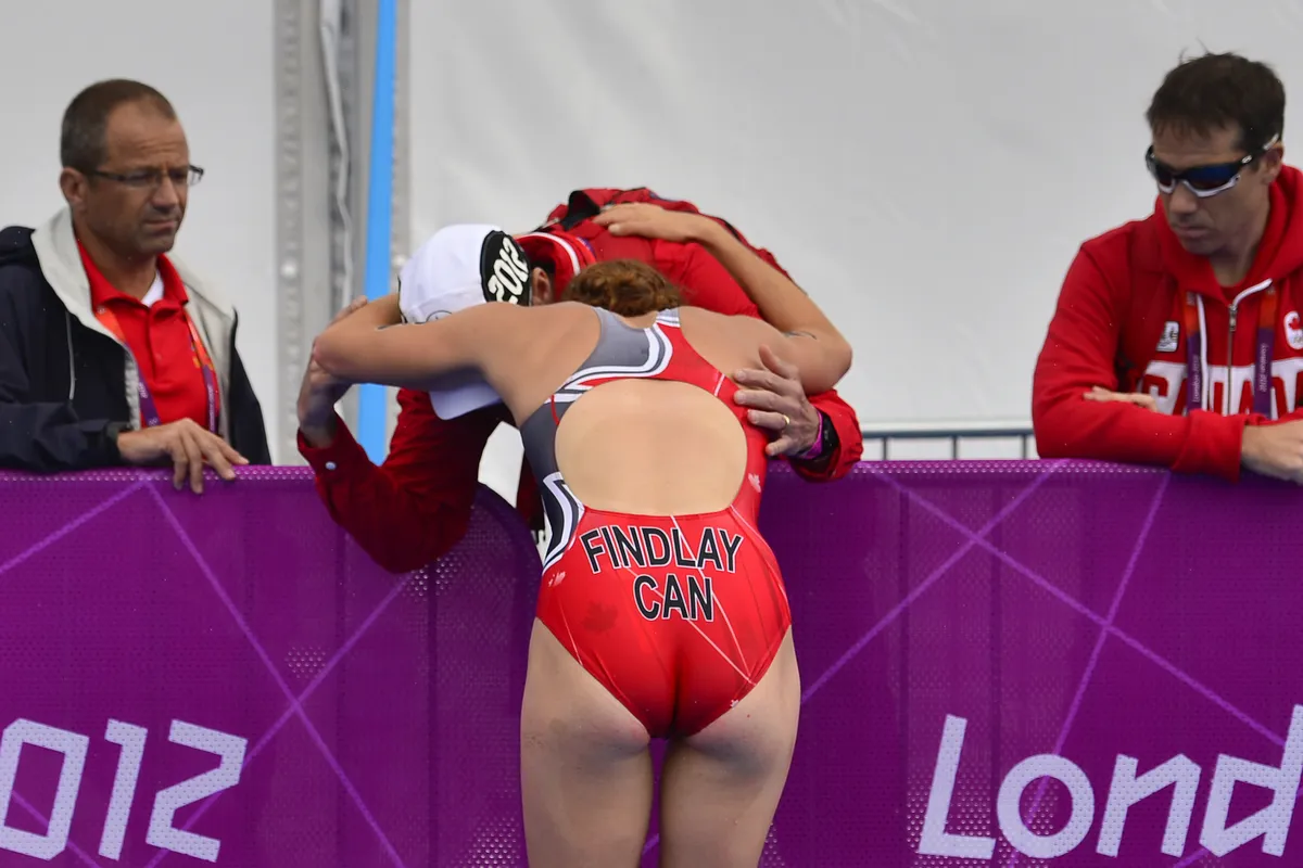 Canada's Paula Findlay is comforted by a coach after finishing the women's triathlon event at Hyde Park at the 2012 Olympic Games in London on August 4, 2012. AFP PHOTO / FABRICE COFFRINI (Photo credit should read FABRICE COFFRINI/AFP/GettyImages)