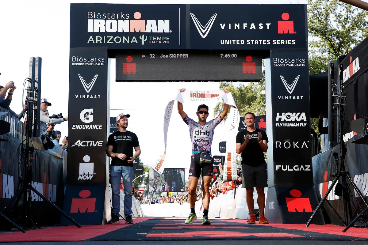 TEMPE, ARIZONA - NOVEMBER 20: Joe Skipper of Great Britain celebrates as he crosses the finish line in first place to win the Men's Professional division at IRONMAN Arizona on November 20, 2022 in Tempe, Arizona. (Photo by Patrick McDermott/Getty Images for IRONMAN)