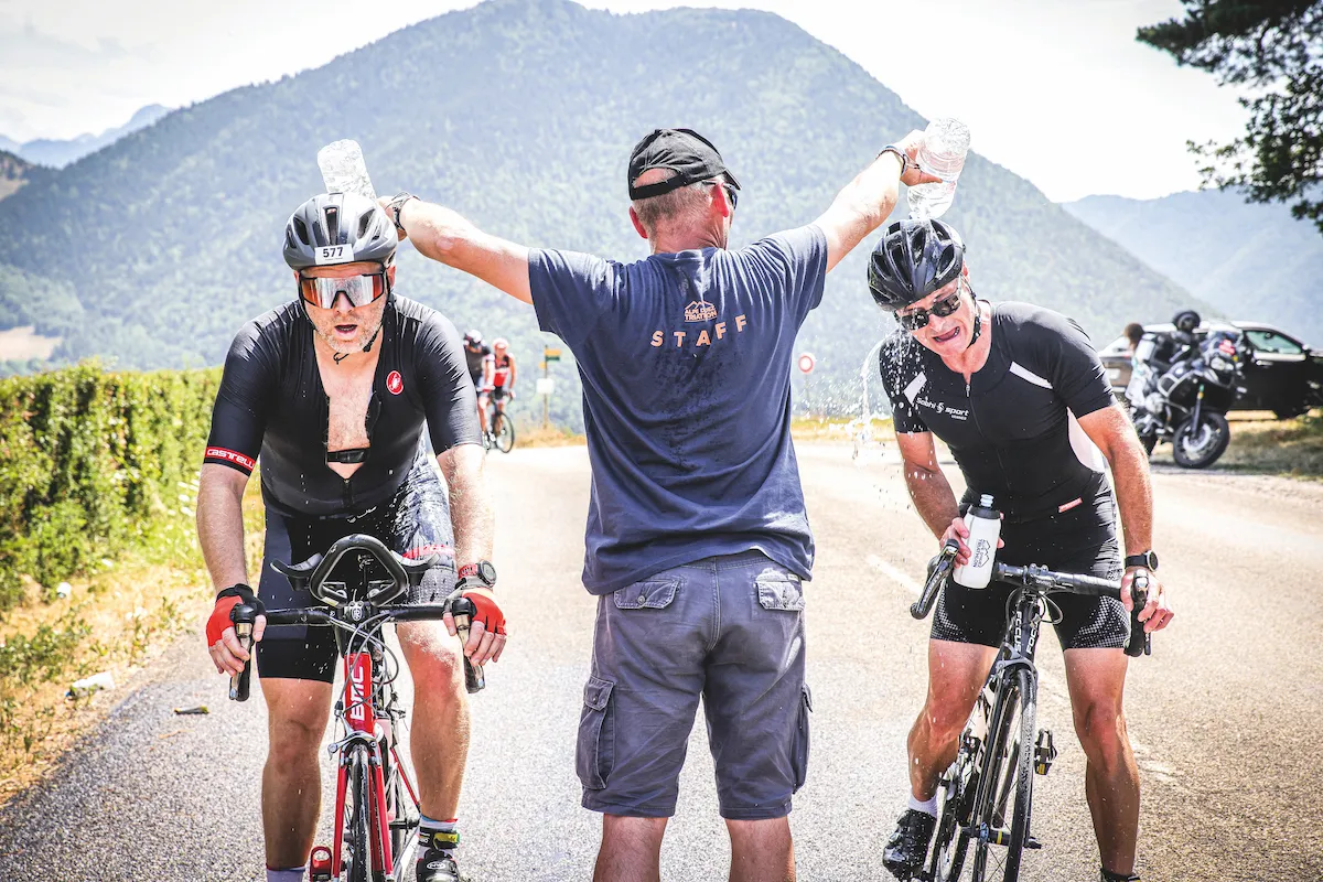 Two male cyclists have water poured over their heads by a volunteer during the Alpe d'Huez Triathlon