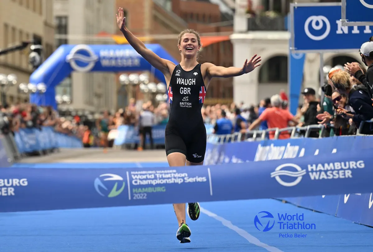GB triathlete Kate Waugh running towards the finish line with arms aloft to give Team GB the mixed team Relay world title, in Hamburg 2022.