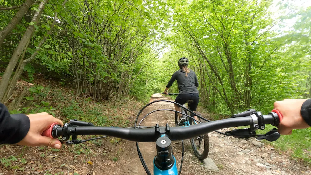 First person perspective of a cyclist as she follows another female biker ahead over a path through the woods