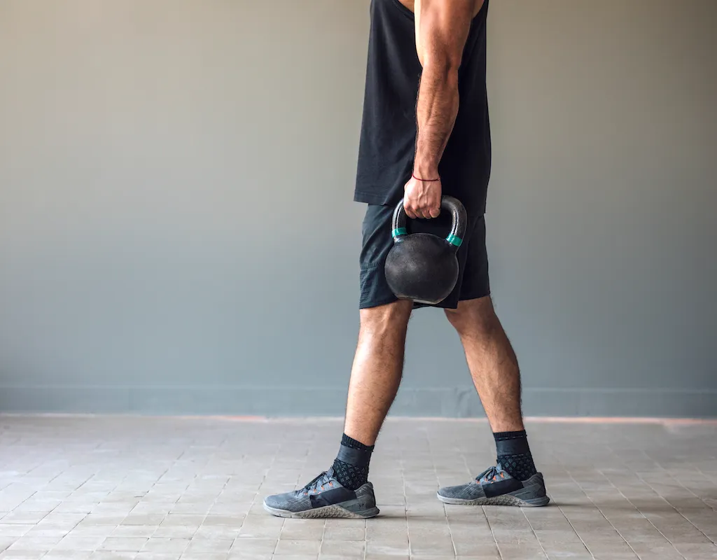 Muscular male athlete doing cross training exercises with kettlebells