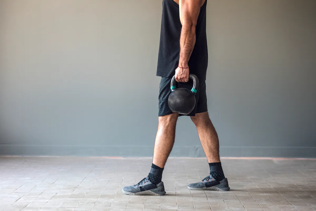 Muscular male athlete doing cross training exercises with kettlebells
