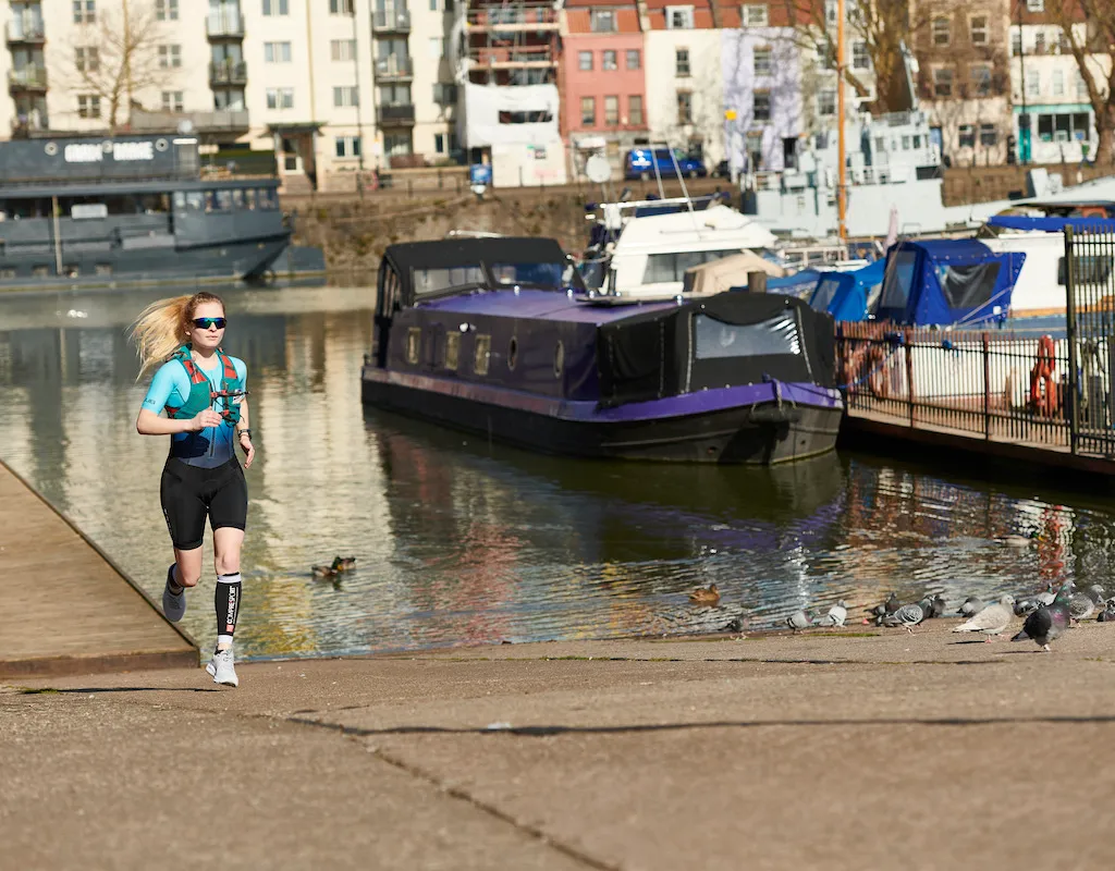 Female runner running alongside water front in Bristol