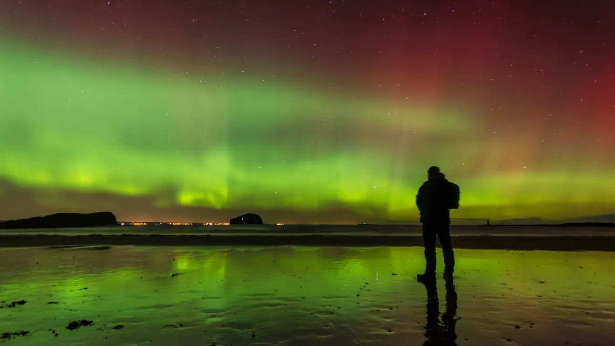 Scotland, East Lothian, silhouette of man standing on Seacliff Beach watching Northern lights