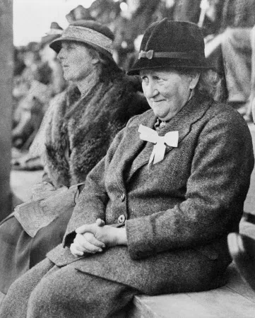 Beatrix Potter sitting outdoors on bench, wearing tweed suit and hat, at Keswick Show -of which she was President, September 1935. Ref. HIL R222. Original photographer unknown - work may be in copyright