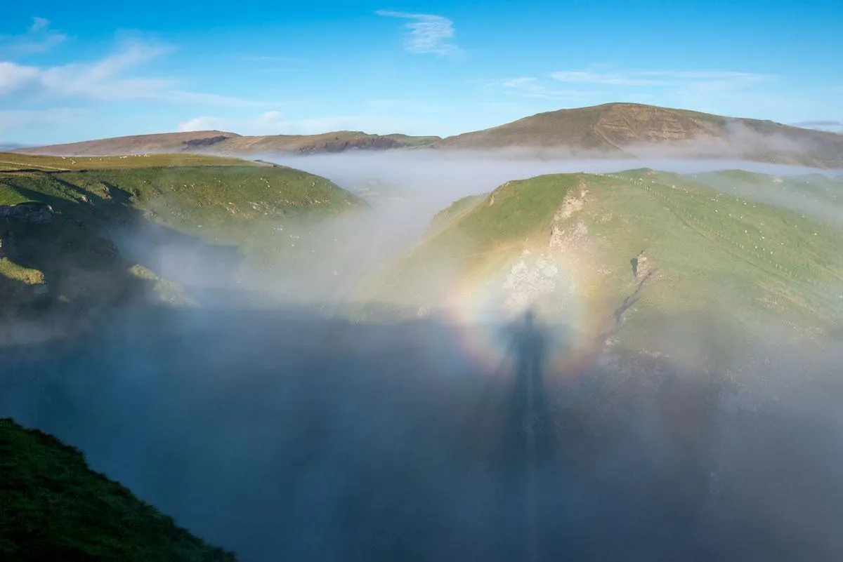 Spectacular misty landscape of Winnats Pass and Mam Tor in Derbyshire. Morning sunlight creating the natural phenomena of a Brocken Spectre. The shadow of the photographer surrounded by a halo in the mist. Credit: R A Kearton/Getty