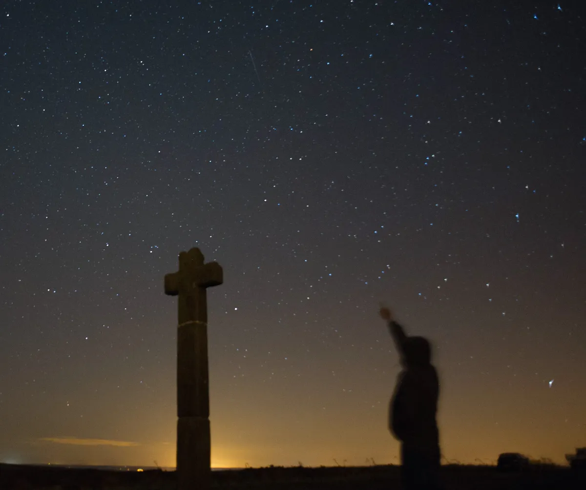 CASTLETON, UNITED KINGDOM - AUGUST 13: James Ritson points skywards as a meteor streaks across the night sky above New Ralph's Cross on August 13, 2013 over the North Yorkshire Moors, United Kingdom. The Perseid Meteor shower is visible from mid-july each year with peak activity being between the 9th and 14th of August. During the peak, the rate of meteors can reach 60 or more per hour. They can be seen all across the sky as they gradually fall away from the tail of the Swift-Tuttle comet. (Photo by Ian Forsyth/Getty Images)