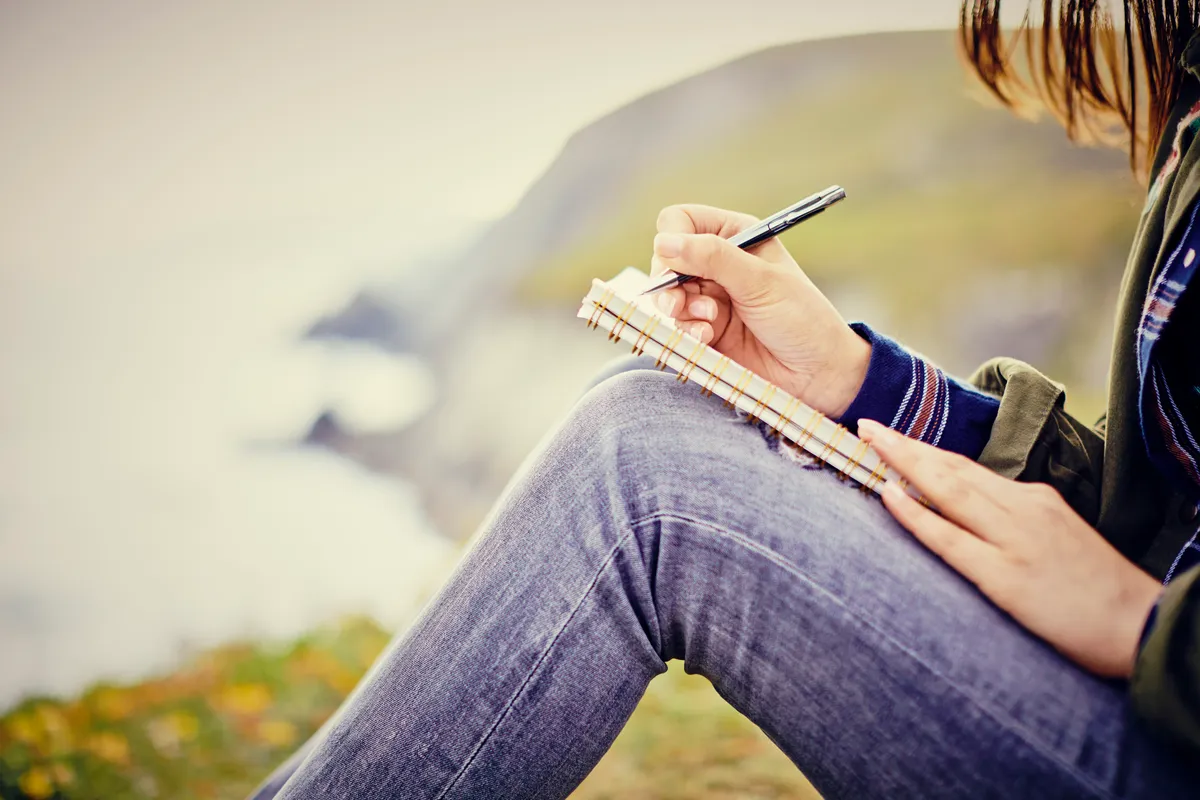Young woman writing in diary while sitting on mountain