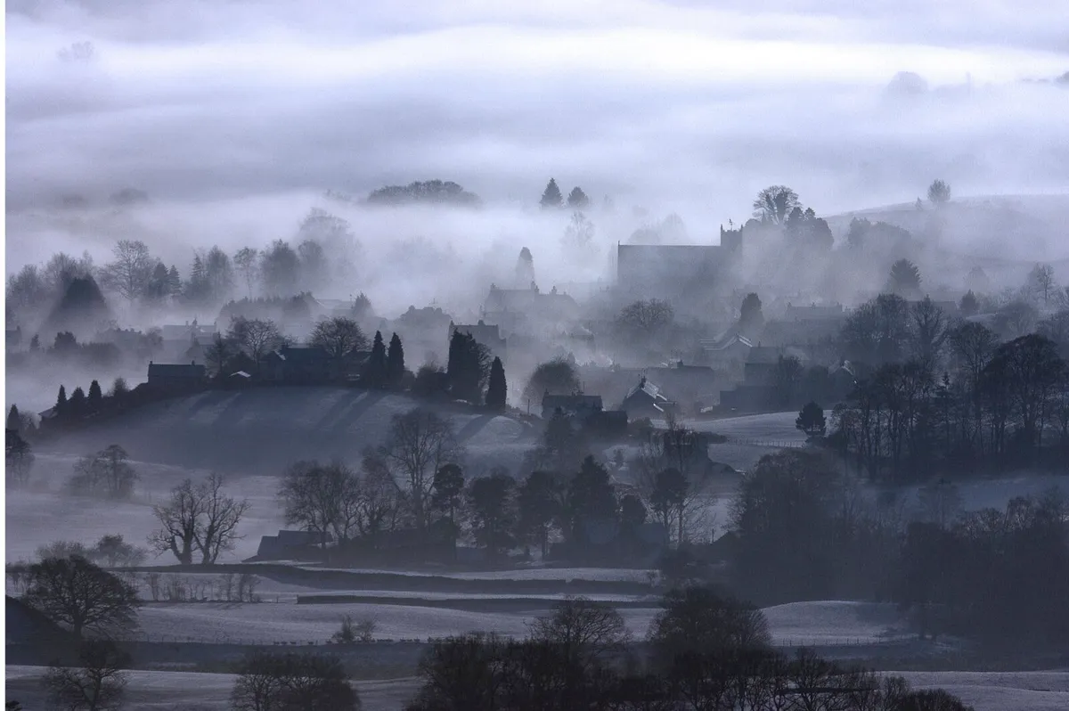An atmospheric view of Hawkshead veiled in mist, taken from the summit of Black Crag above Tarn Hows in winter.