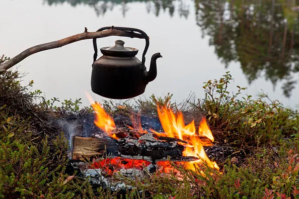 Blackened tin kettle boiling water over flames from campfire during hike along lake. (Photo by: Arterra/UIG via Getty Images)