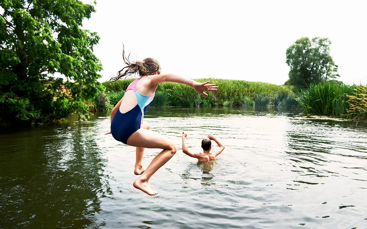 Two children swimming in a river with one child jumping in