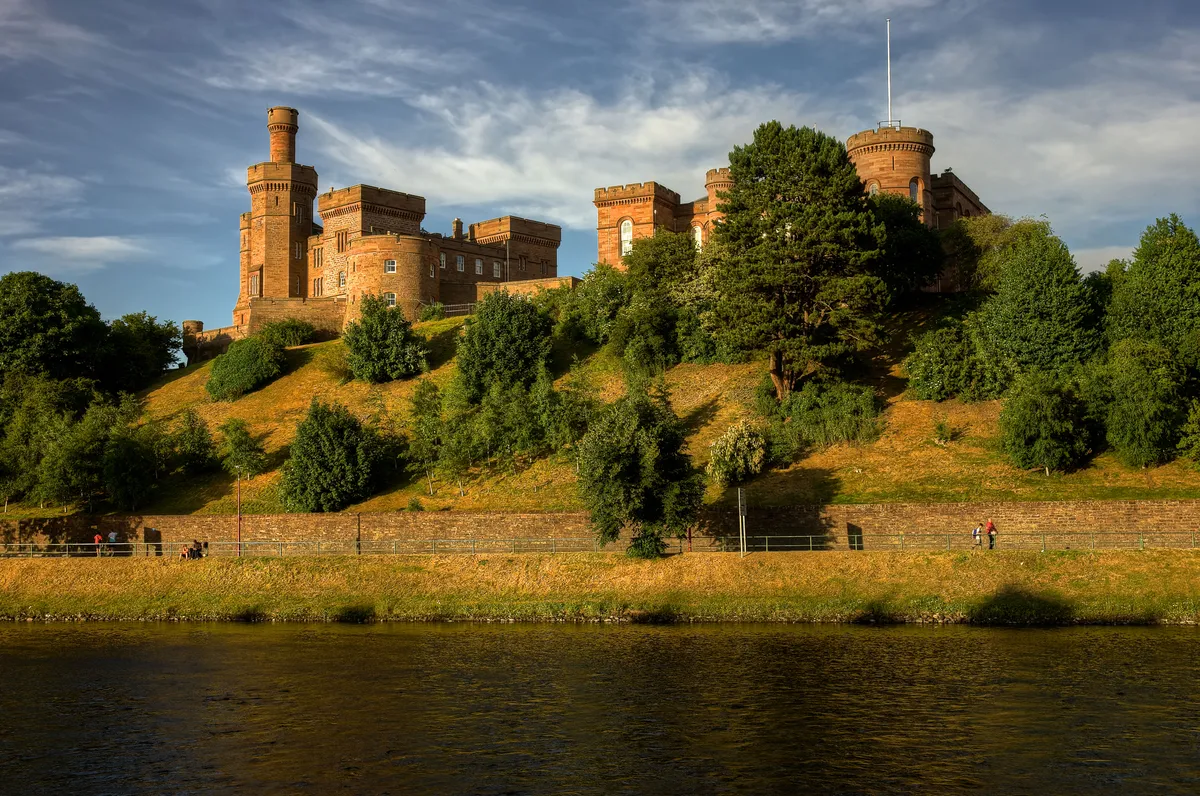 Inverness Castle, Scotland surrounded by trees with a river in the foreground