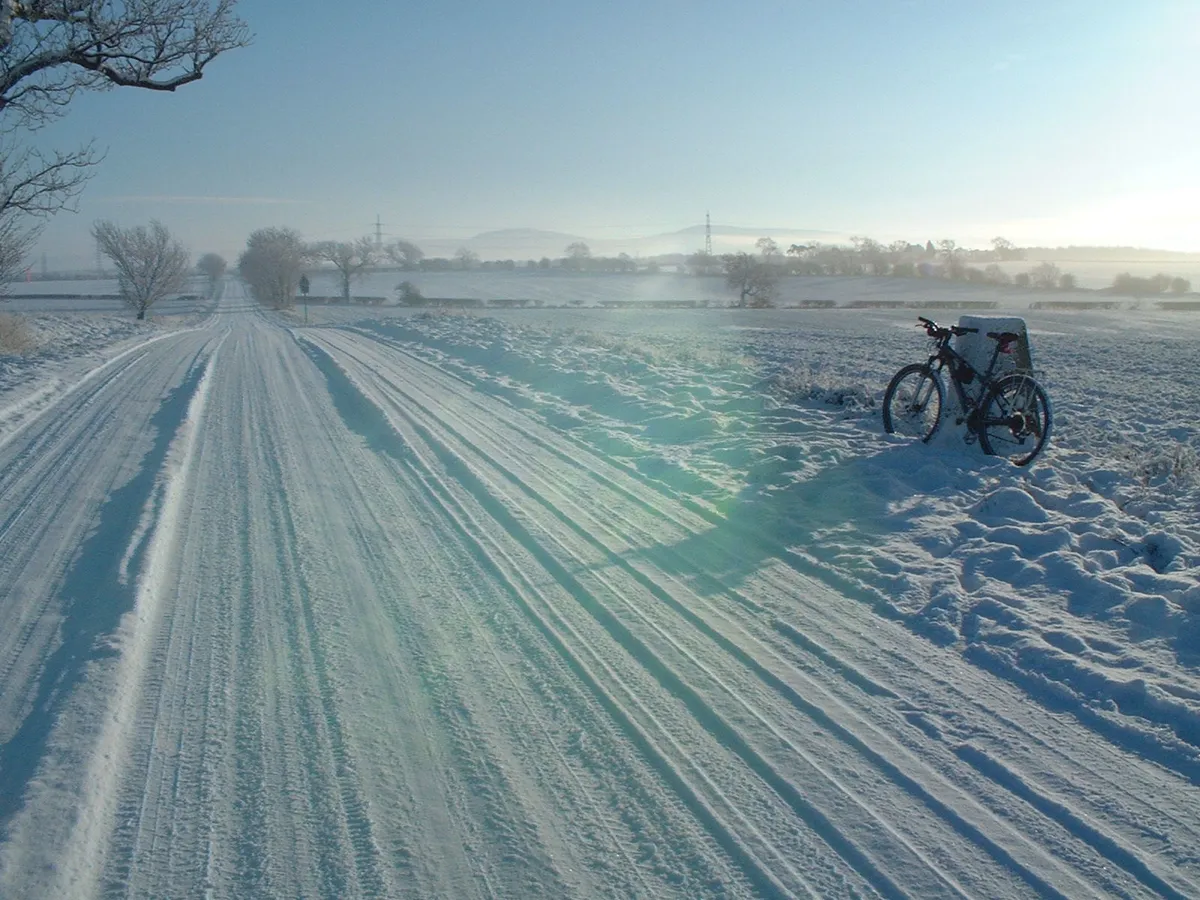 Darlington, on a snowy day, cycle propped on a milestone on National Route 1