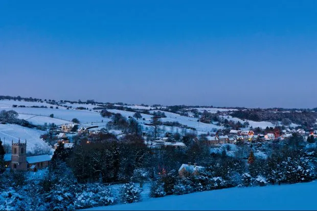 Idyllic winter village church cottages snow covered landscape Cotswolds UK