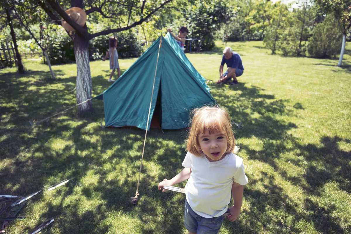 Family assembling camping tent and playing camping in back yard.