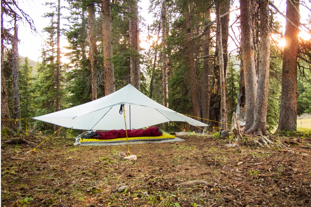 A backpacking camp scene with a tarp tent and sleeping bag in the trees. Photo taken during a backpacking trip into the Weminuche Wilderness around the Rio Grand Pyramid peak, Colorado.
