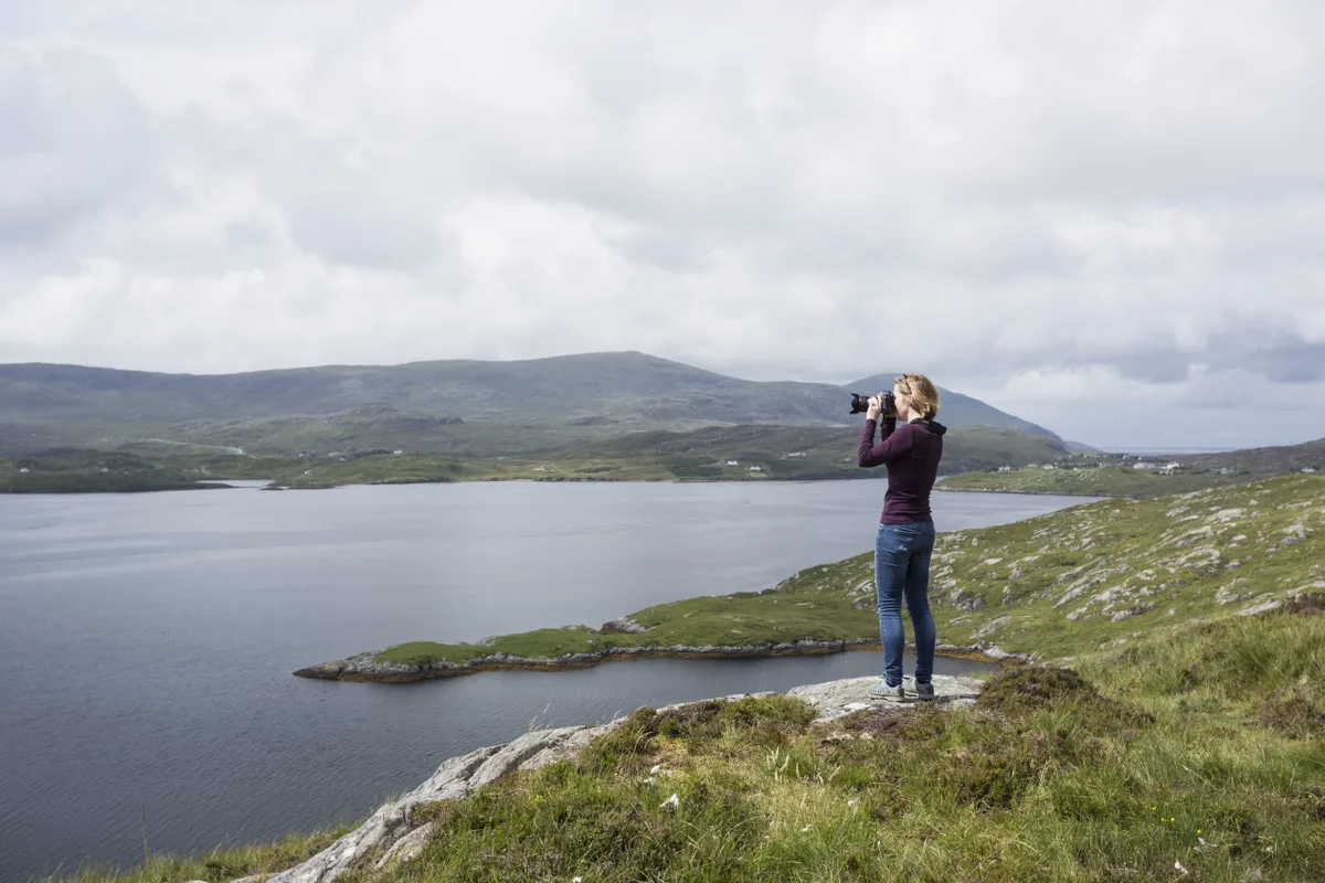 Woman photographing view, standing on north shore of East Loch Tarbet, North Harris, Outer Hebrides, Scotland