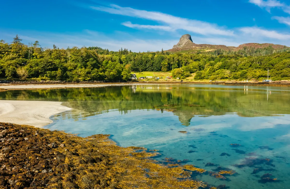 Isle of Eigg, Small Isles, Scotland. Beautiful bay in Summer with blue sky and An Sgurr reflected in the clear blue waters