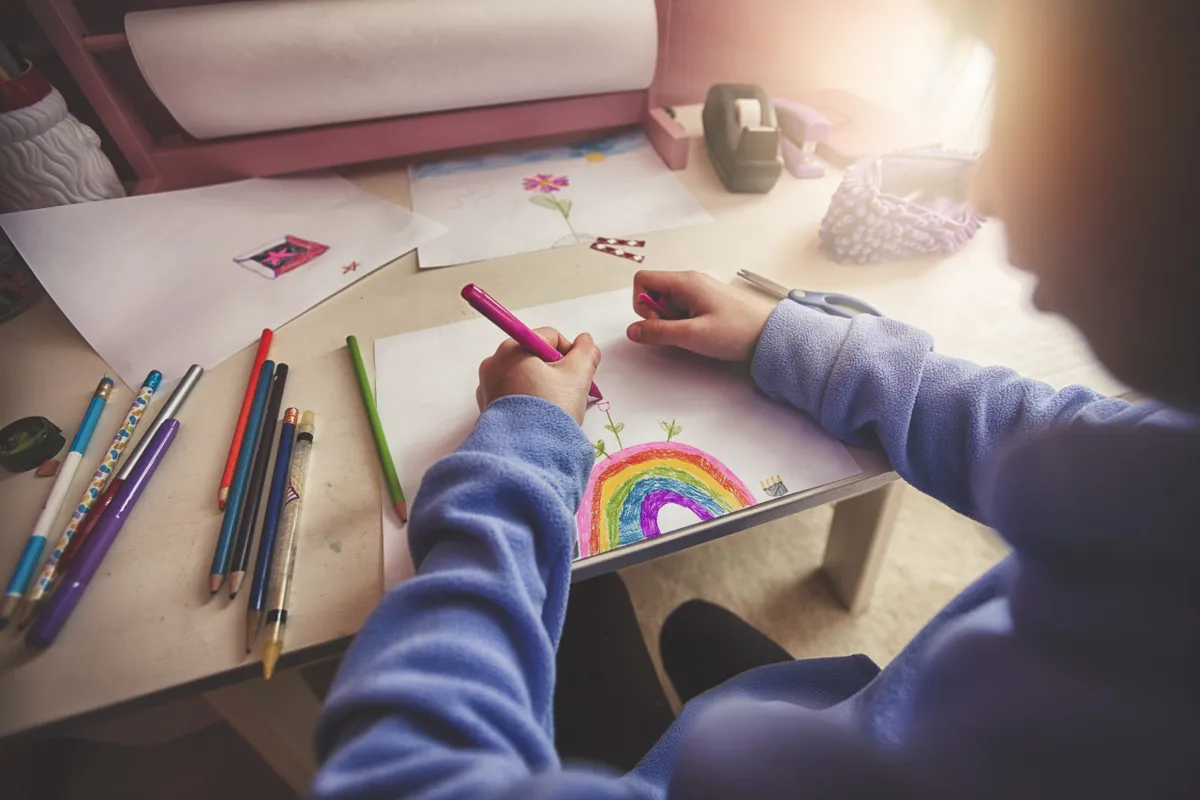 girl drawing a rainbow her desk