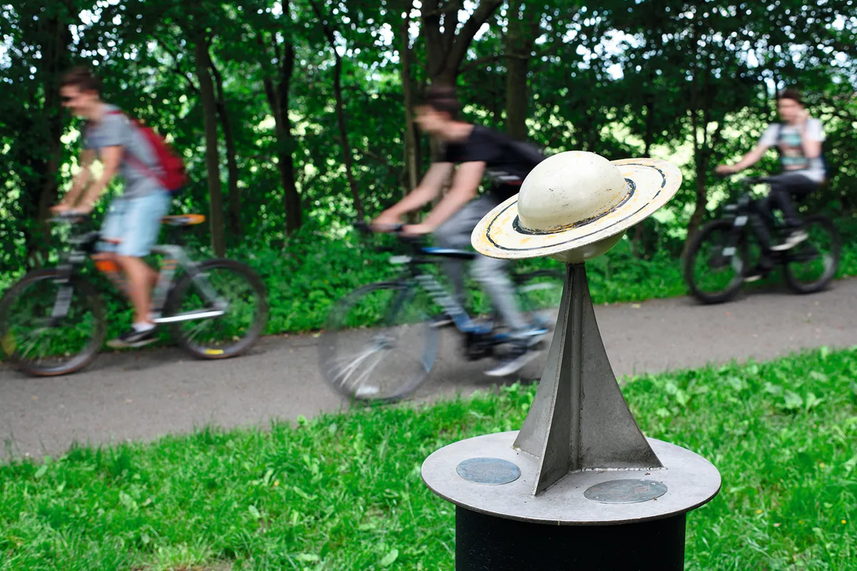 Cyclists pass a model of the planet Saturn