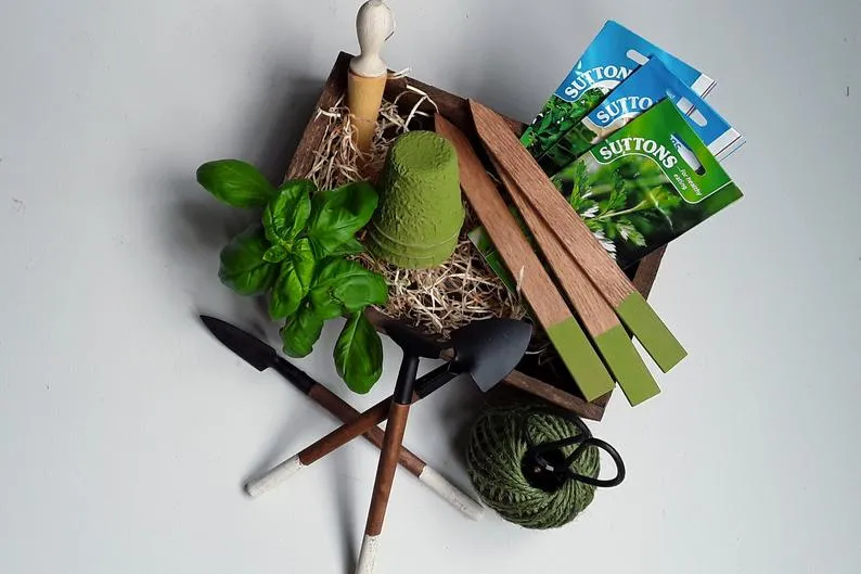 A gift set including twine and scissors, mini gardening tools, a dibber, wooden markers, pots and seeds in a wooden trough.