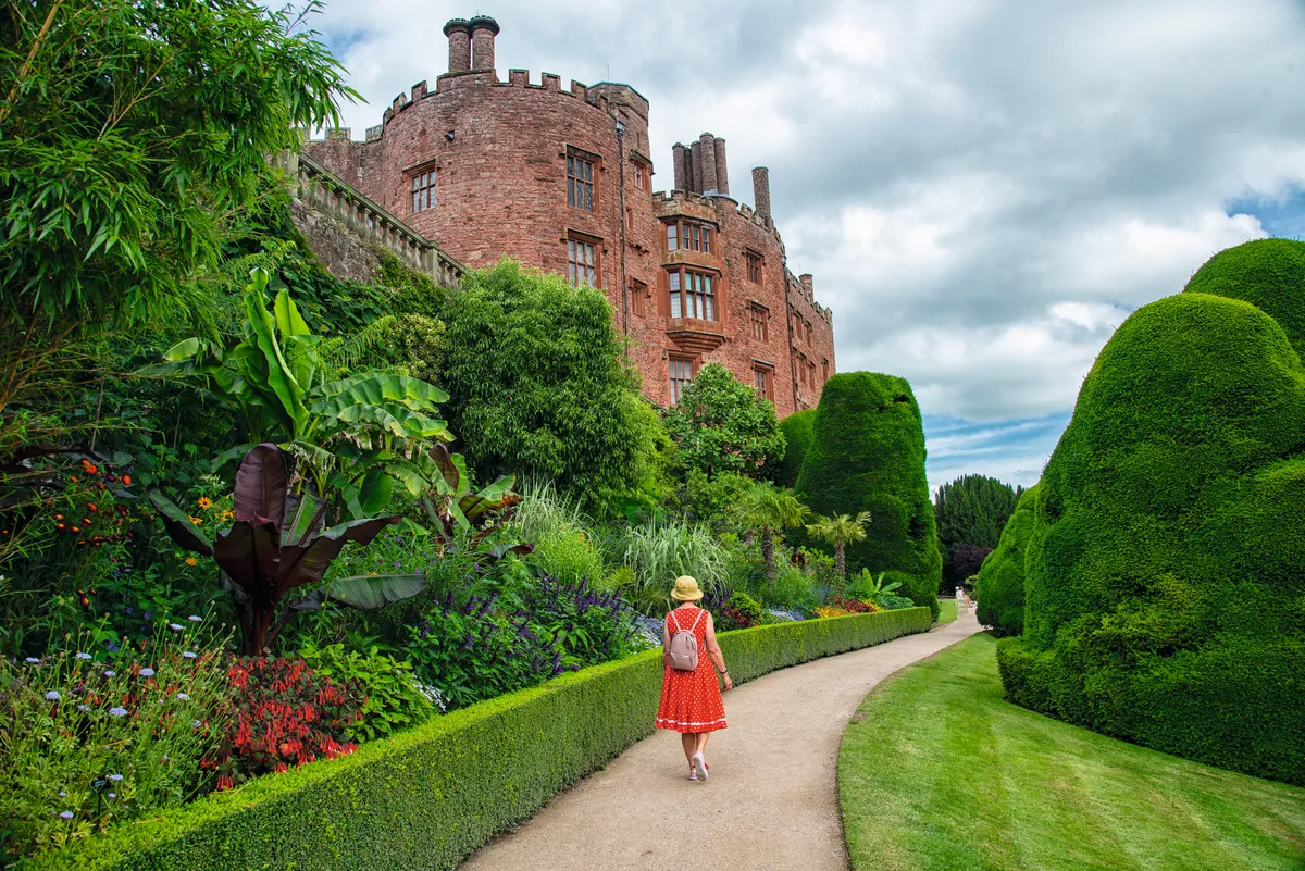 Woman walking through gardens by castle