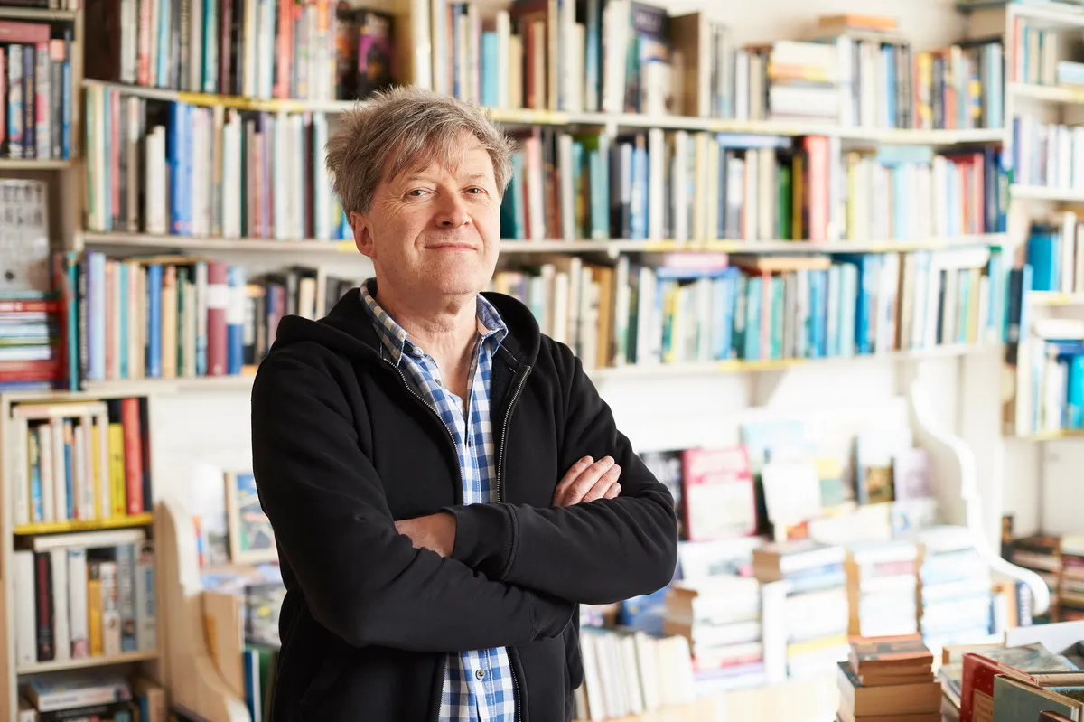 A man stands purposefully looking at the camera with rows of secondhand books behind