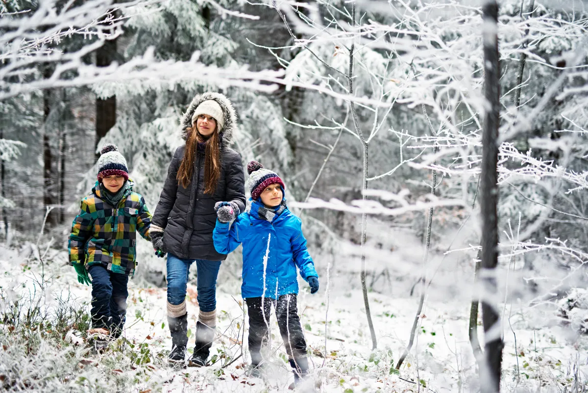 Sister with little brothers walking in frozen winter forest