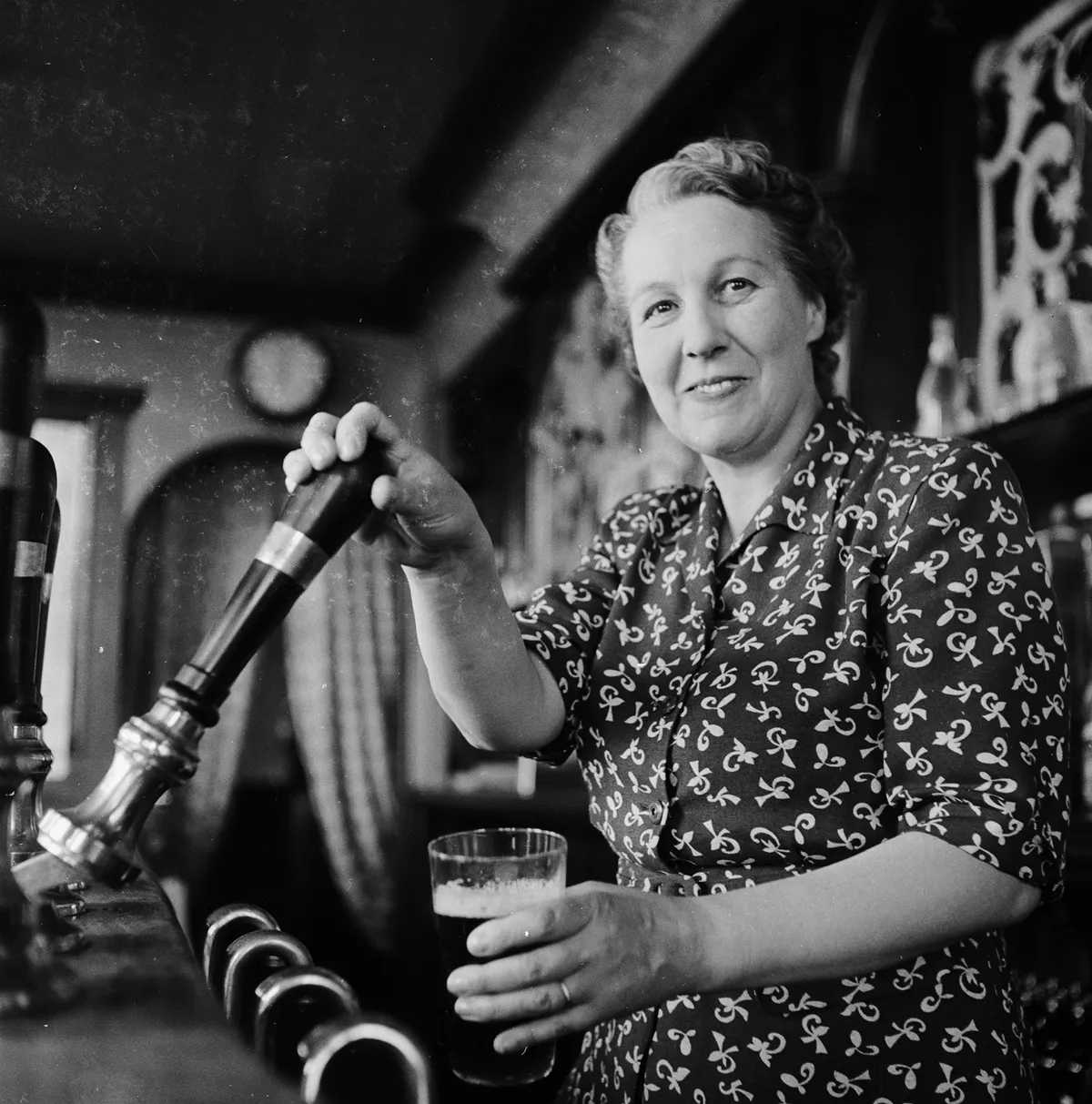 Black and white image of a cheerful woman pulling a pint of ale
