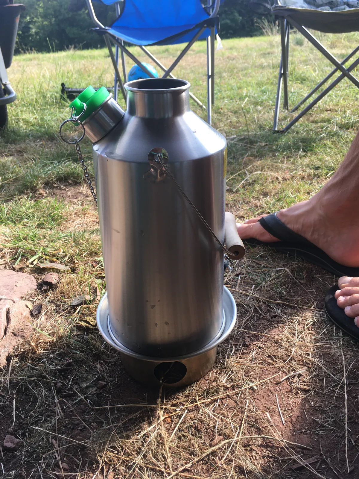 Stainless steel Kelly Kettle with green whistle stopper in a field with camping chair in background