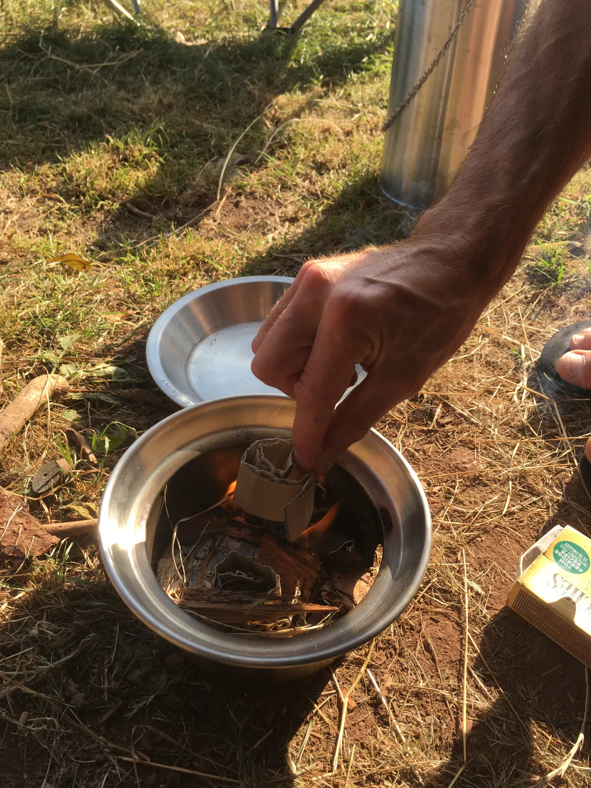 Person lighting a small fire in a Kelly Kettle fire base using bits of dry twigs and paper