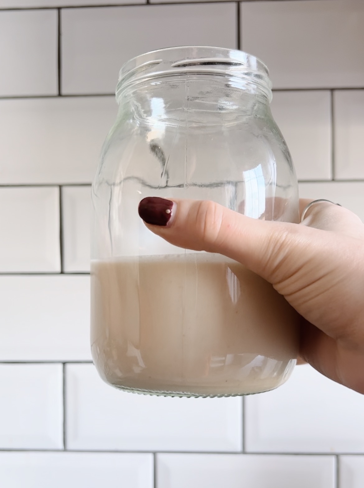 glass of homemade oat milk with white tiled background