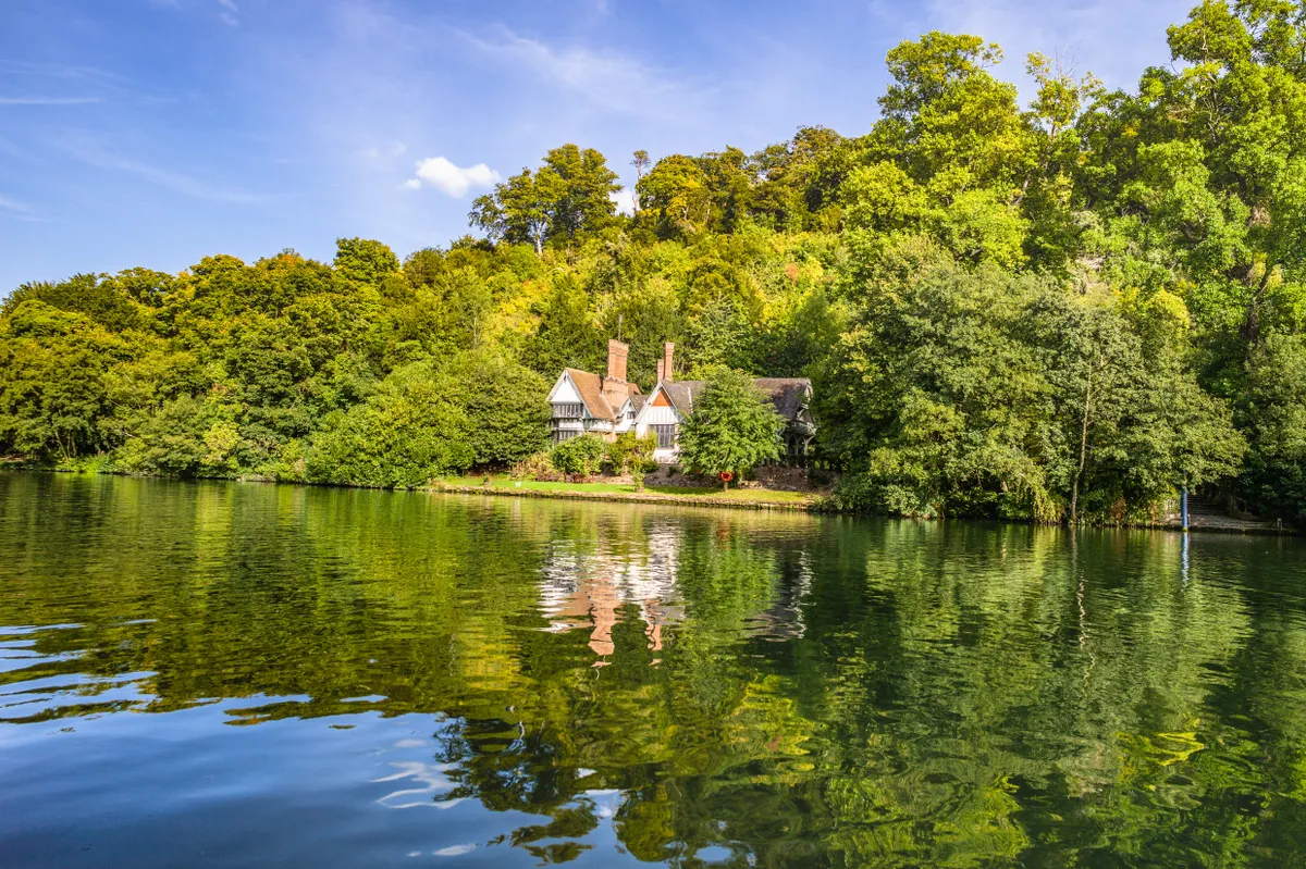Spring cottage on the riverbank in the estate of the National Trusts Cliveden house with blue sky and mirror reflection in the water