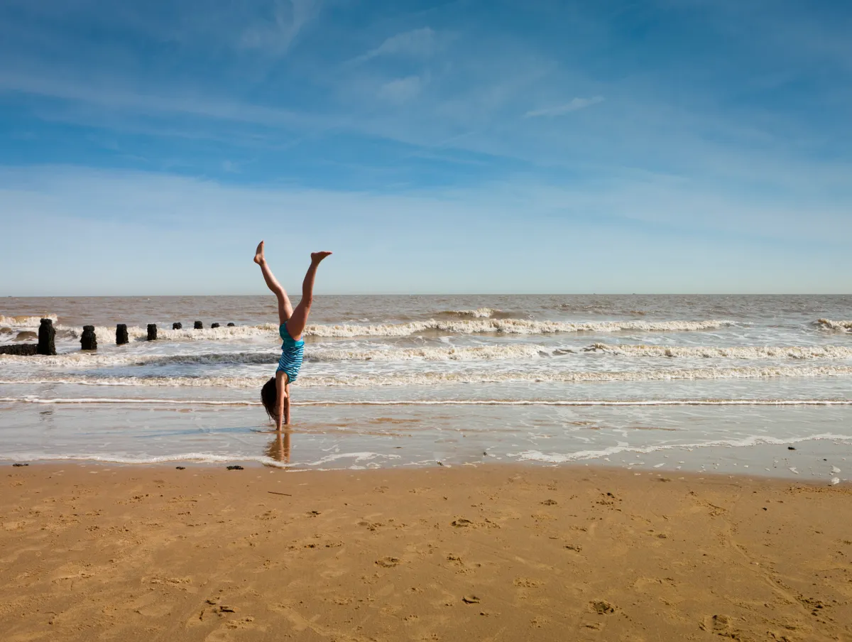 A girl doing a handstand on a beach on a sunny day in Frinton in Essex