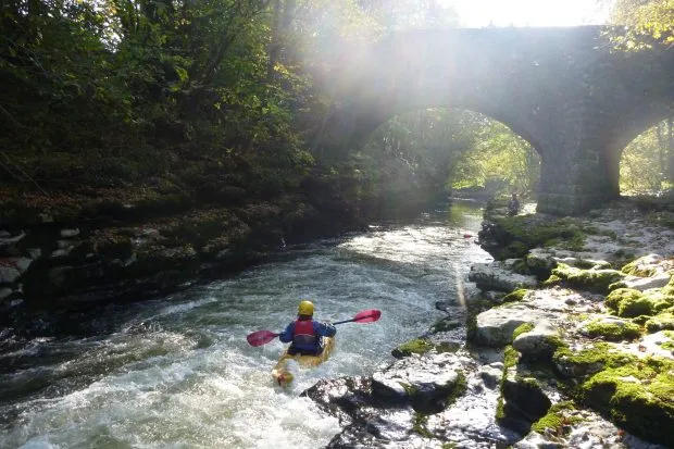 Kayaker paddling beneath Hawes Bridge on the River Kent on a sunny day