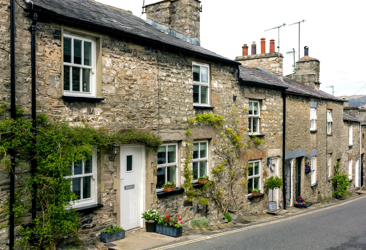 View of a row of stone cottages with planted containers outside. There are no people in the photograph.
