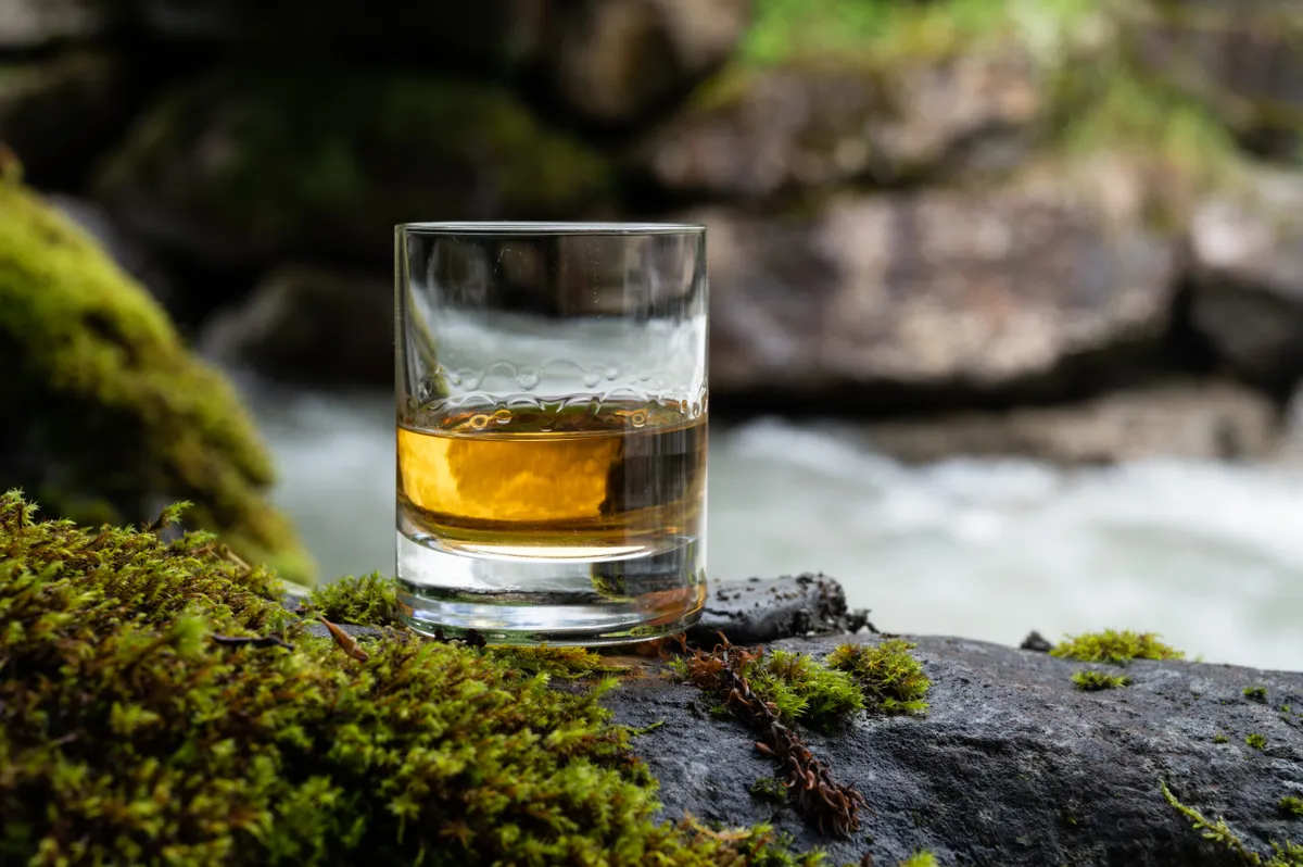 Glass of strong scotch single malt whisky with fast flowing mountain river in background