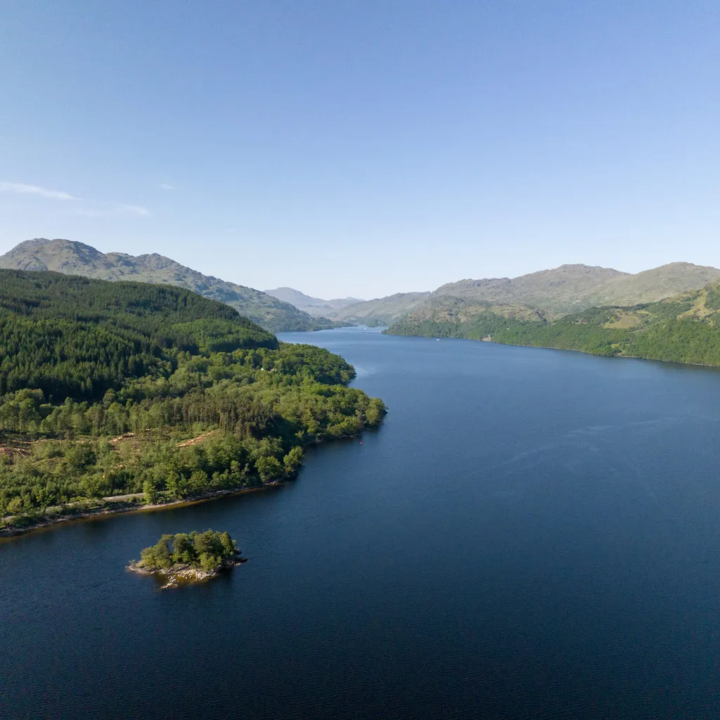 Drone image of Loch Lomond with trees and blue sky