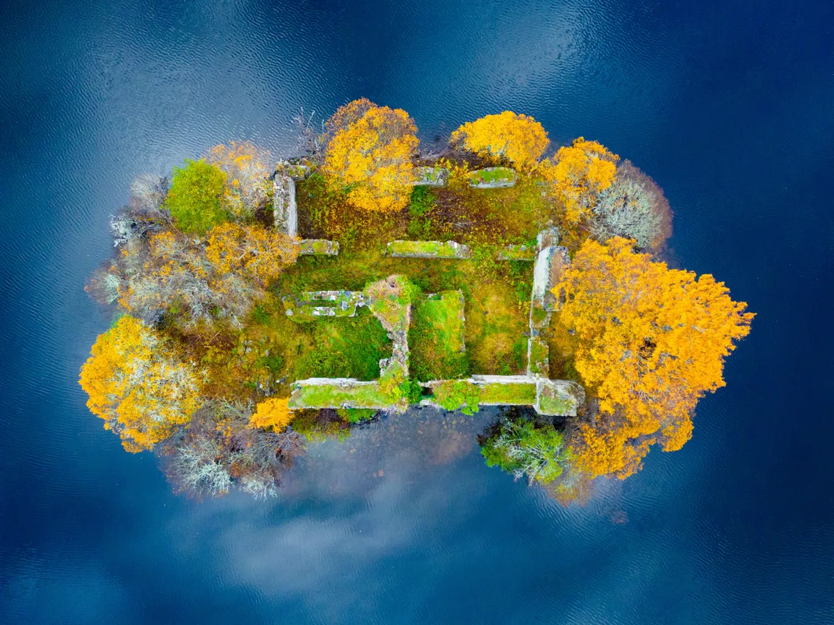 Aerial view of spectacular late autumn colours and reflections of clouds around ruined castle on island on Loch an Eilein in the Rothiemurchus estate in Cairngorms National Park near Aviemore in Scottish Highlands