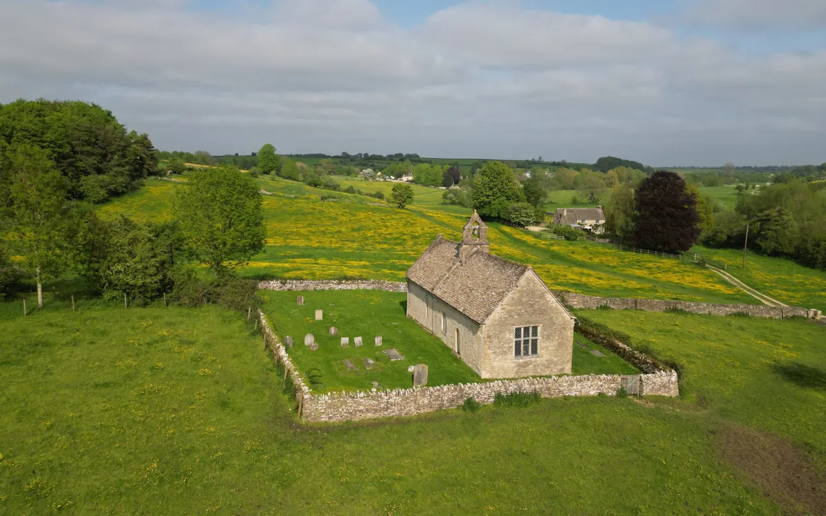 An aerial view of St Oswalds Church Widford in a lush green un der the blue sky