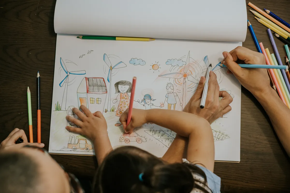 Girl drawing house with solar panels and wind turbines with coloured pencils