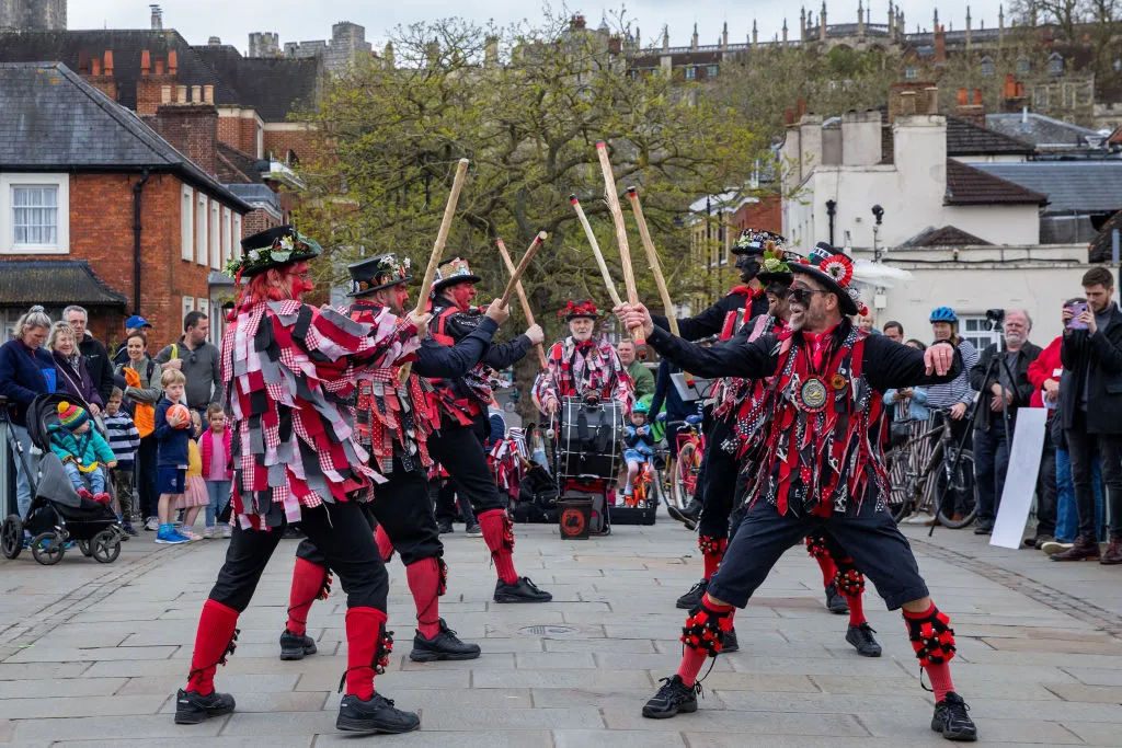 Morris dancers wearing red and black and holding sticks dance on Windsor Bridge on May Day