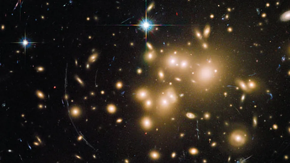 A Hubble Space Telescope image showing gravitational lensing in action. At the centre of the image is a galaxy cluster, which contains so much dark matter mass its gravity is bending the light of more distant objects (seen as curves of light around the cluster). Image Credit: NASA, ESA, J. Richard (CRAL) and J.-P. Kneib (LAM). Acknowledgement: Marc Postman (STScI)