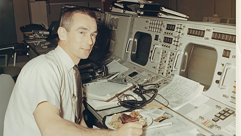 Gene Cernan, who would eventually become the last of the Apollo astronauts to set foot on the Moon, grabs a rare moment of sustenance amongst the hubbub of Mission Control.